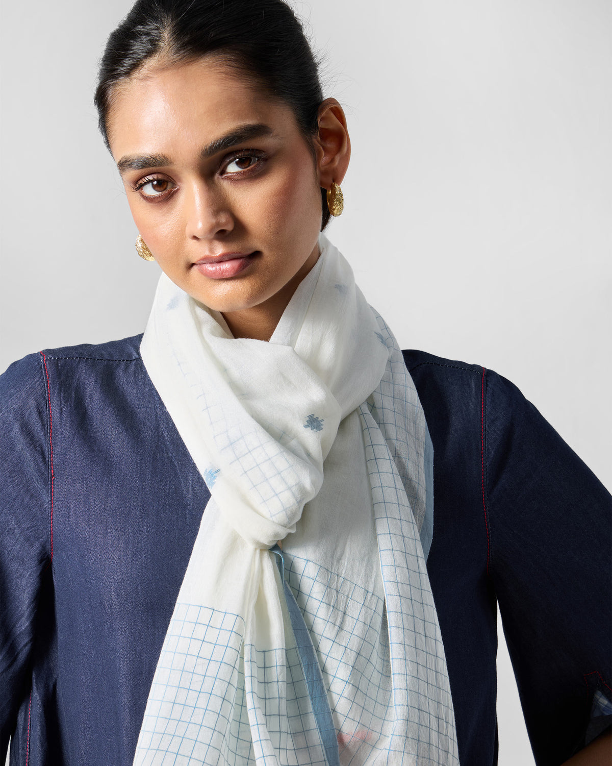 Person wearing the Checked Skies scarf in white with blue checks and small blue motifs.