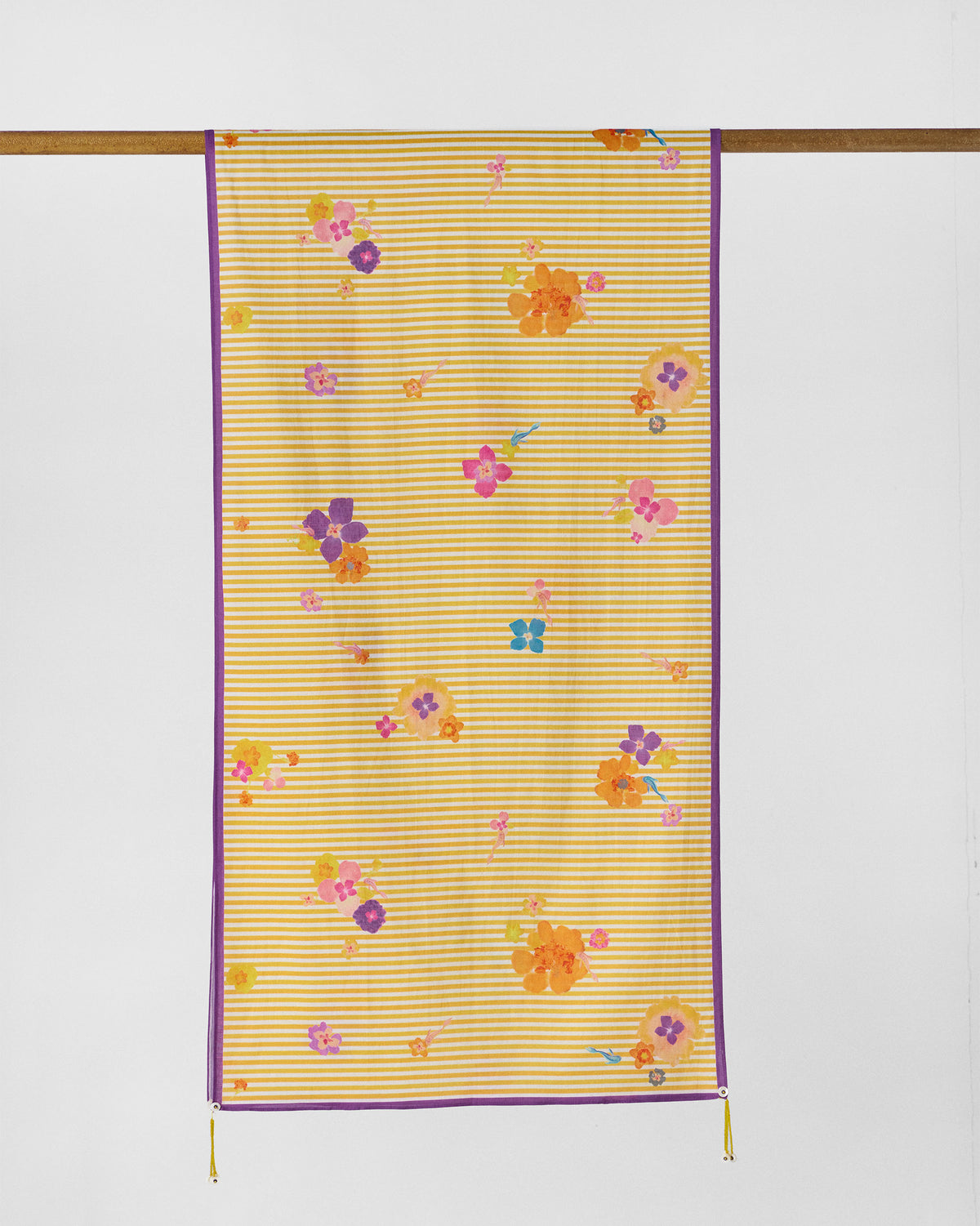 Full Basant Bloom scarf hung from a rod, yellow stripes with a purple border and flowers.