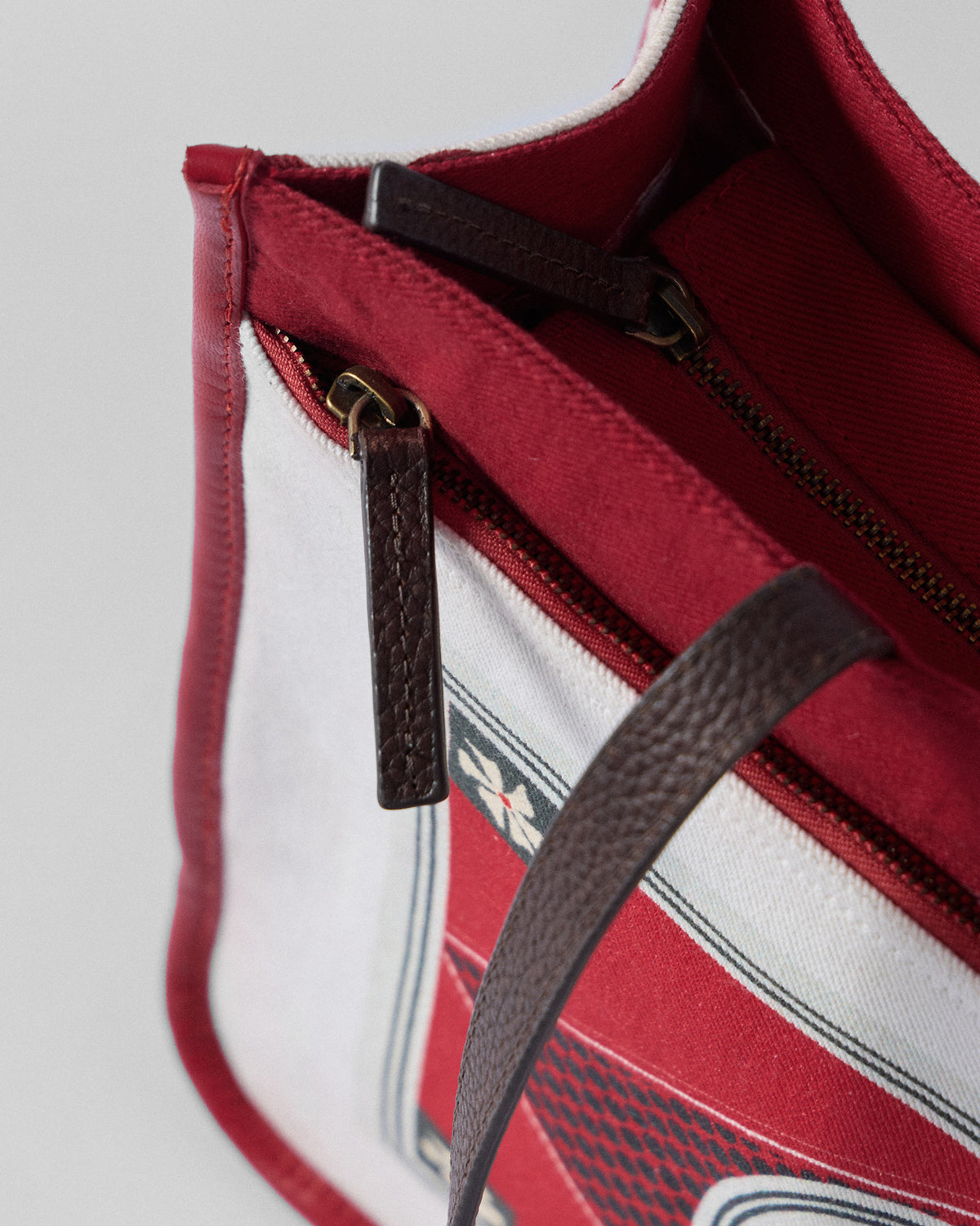 Close-up of the leather strap and zip on an ivory and red Ganges tote.