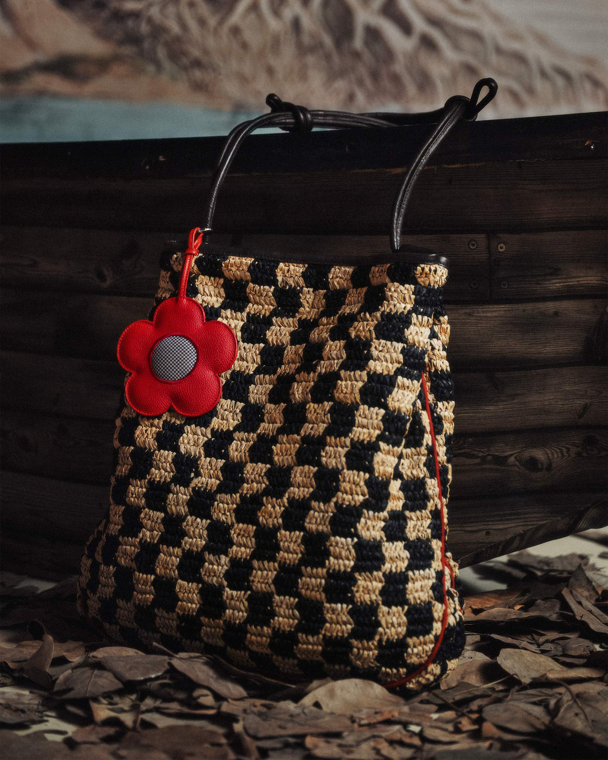 Black and natural Nomad Tote with a red flower charm on fallen leaves.