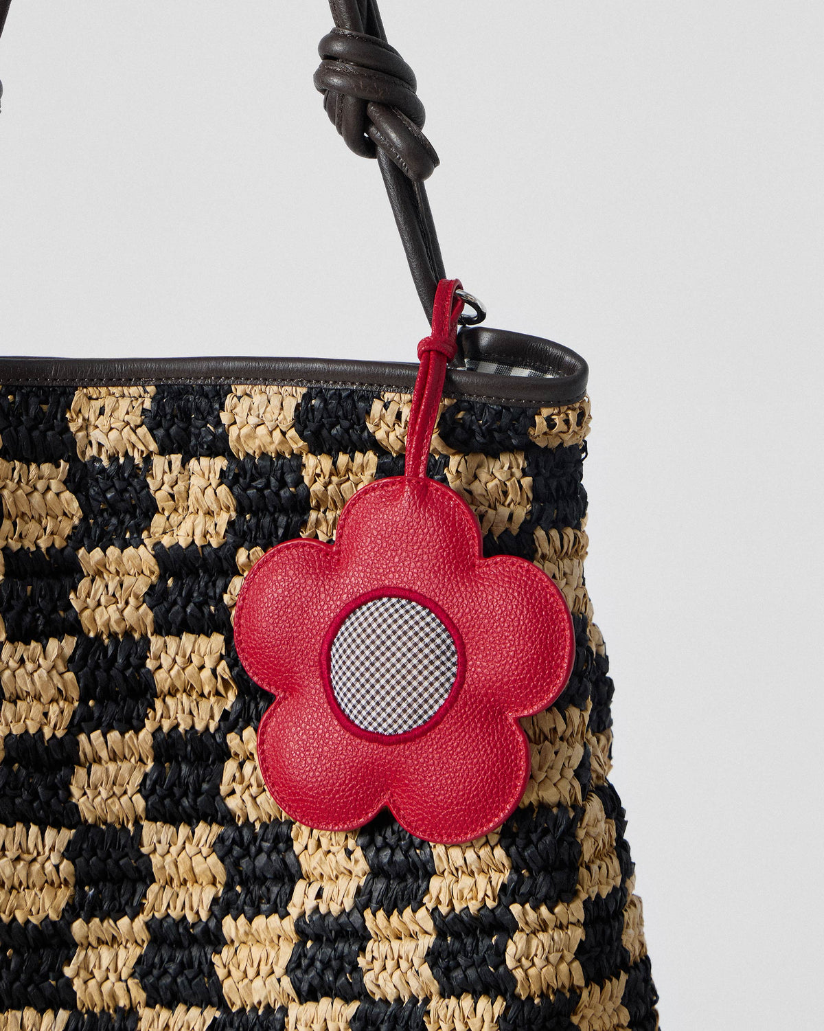 Close-up of the red flower charm on a black and natural Nomad Tote.