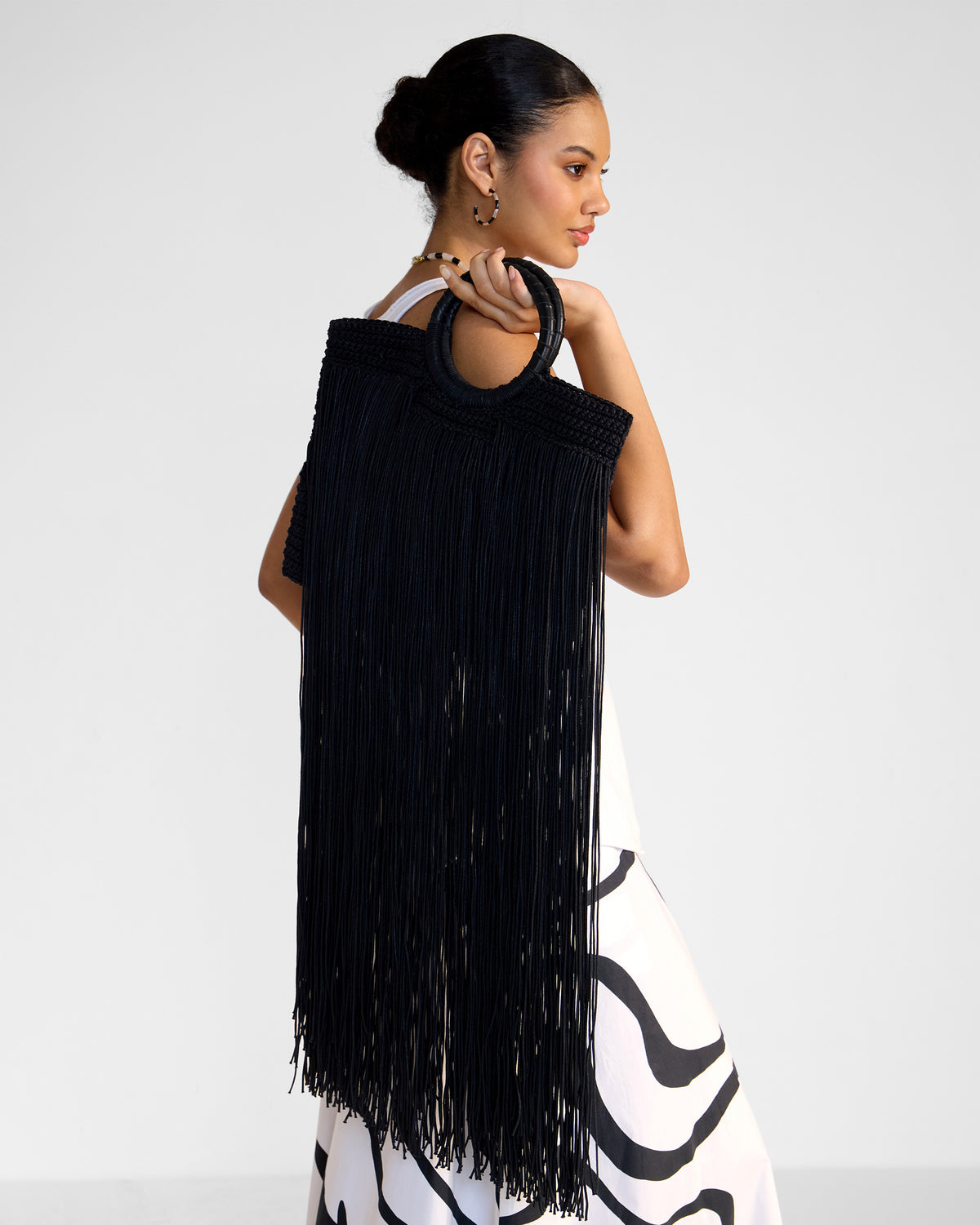 Black braided fringe bag with a circular handle worn on a shoulder.