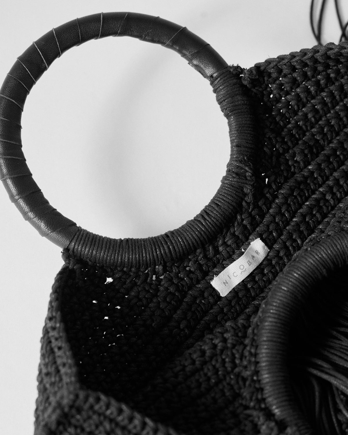 Close-up of a black crochet fringe bag opening with a Nicobar label.