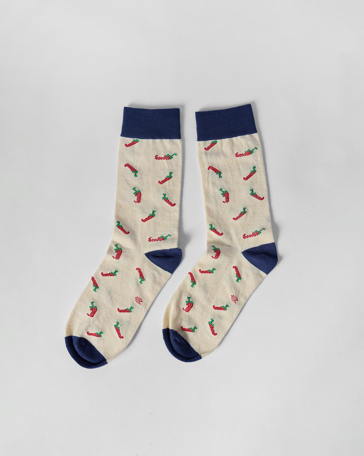 Pair of Chilli Pop socks laid flat, ivory with a red chilli print and navy cuffs.