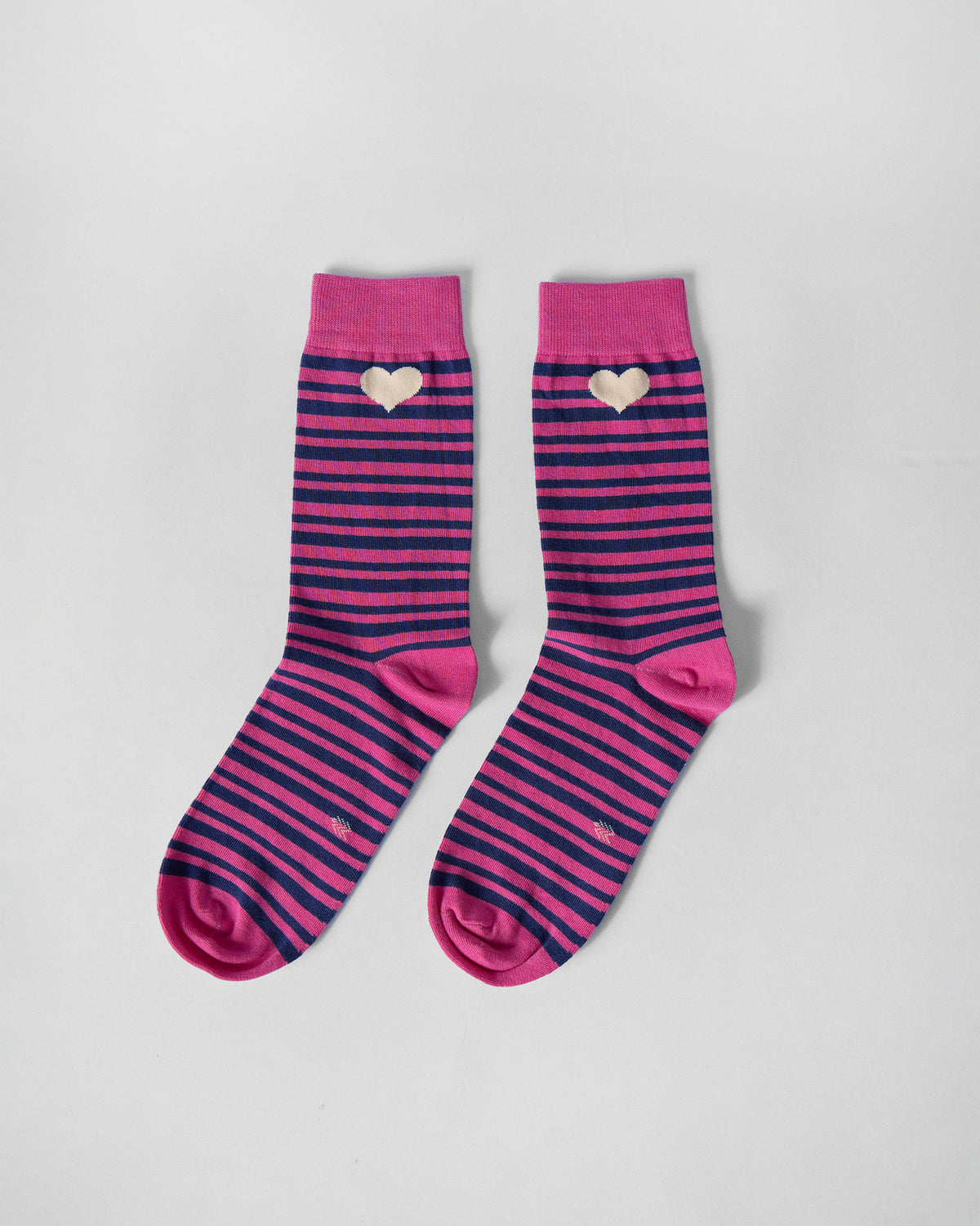 Pair of pink and navy striped Thick & Thin socks with cream hearts laid flat.