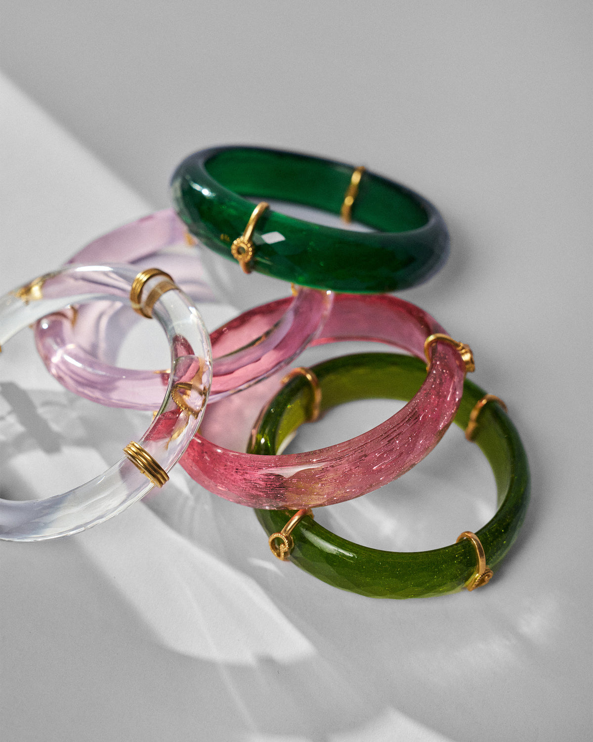 Overlapping stack of translucent pink and green Baraat bangles with gold wraps.
