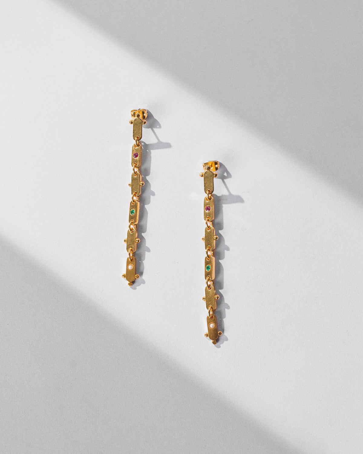 Pair of long gold Ladder earrings with coloured glass laid flat.
