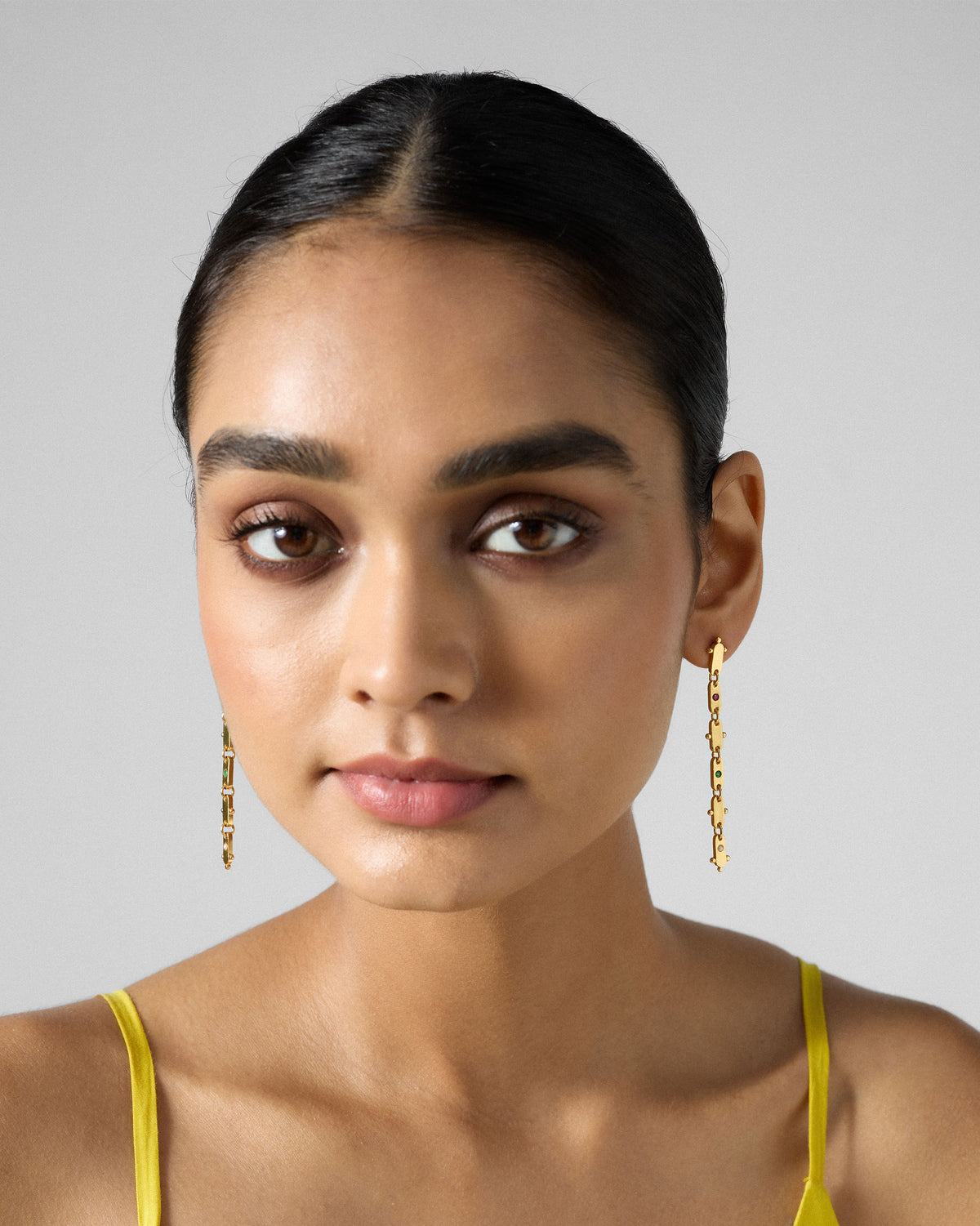 Person wearing long gold Ladder earrings with coloured glass.