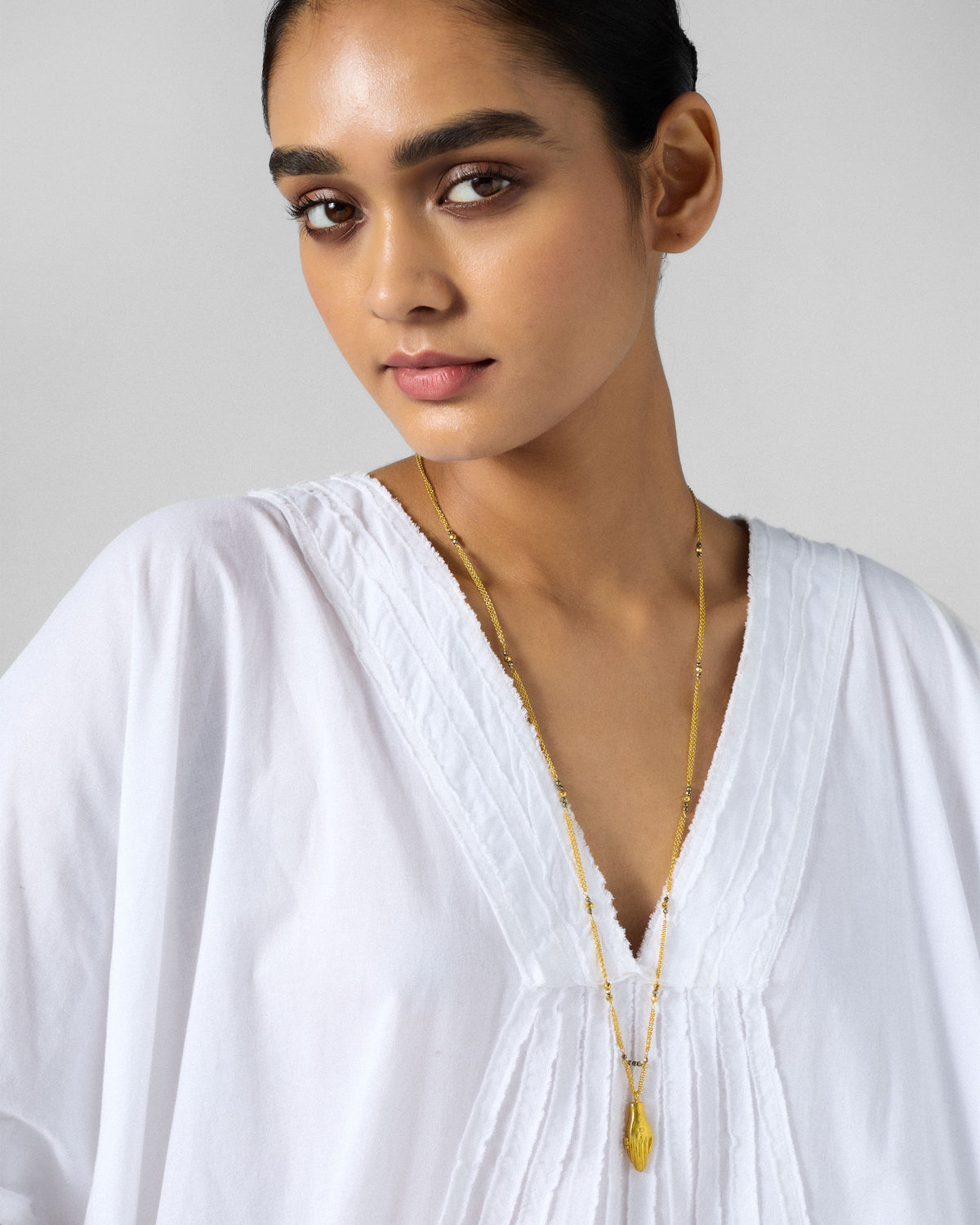 Gold Sama necklace worn long with a hand pendant and dark beads.