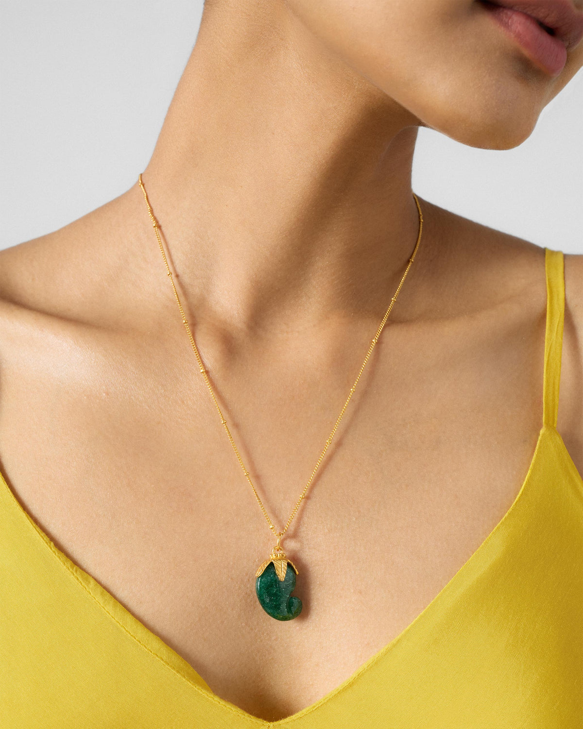 Gold Ambi necklace with a green mango pendant worn at the neck.