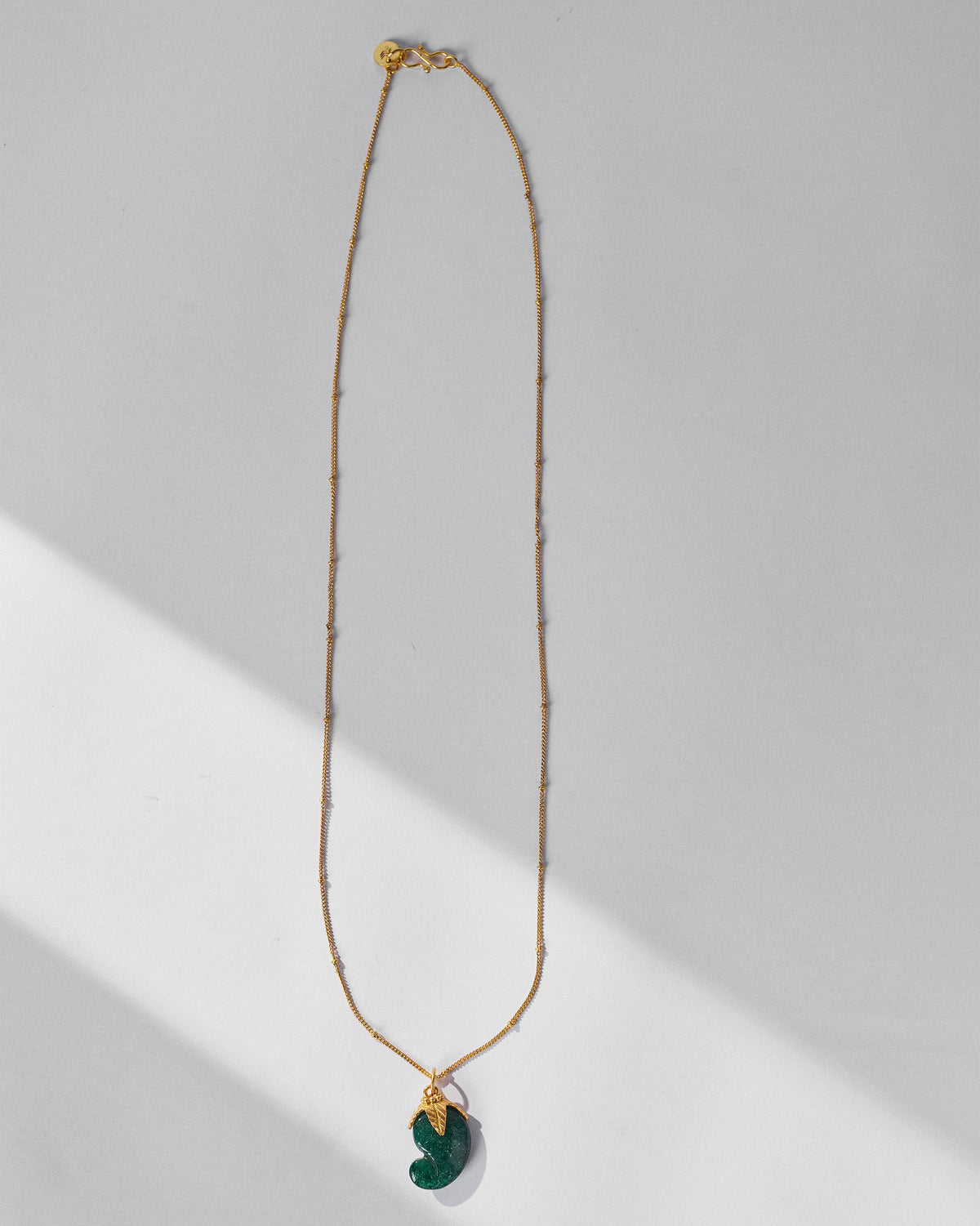 Long gold Ambi necklace with a green mango stone pendant.