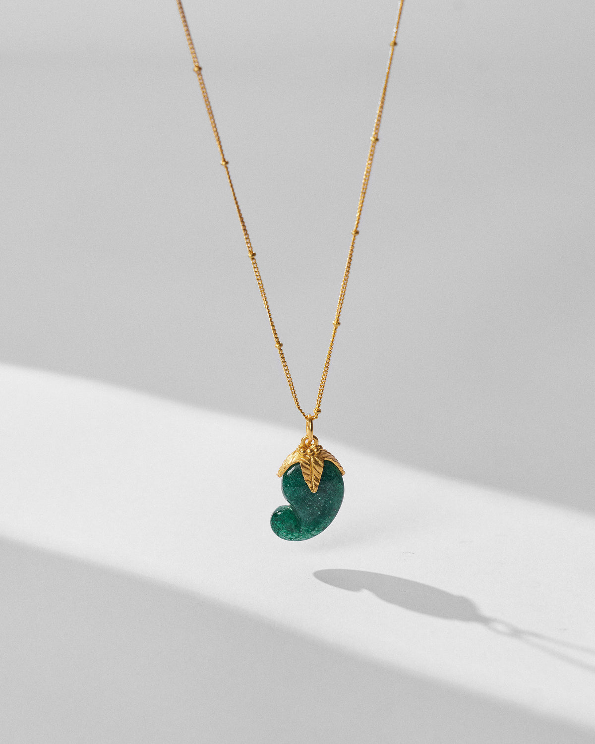 Gold Ambi necklace hanging with a green mango stone pendant.