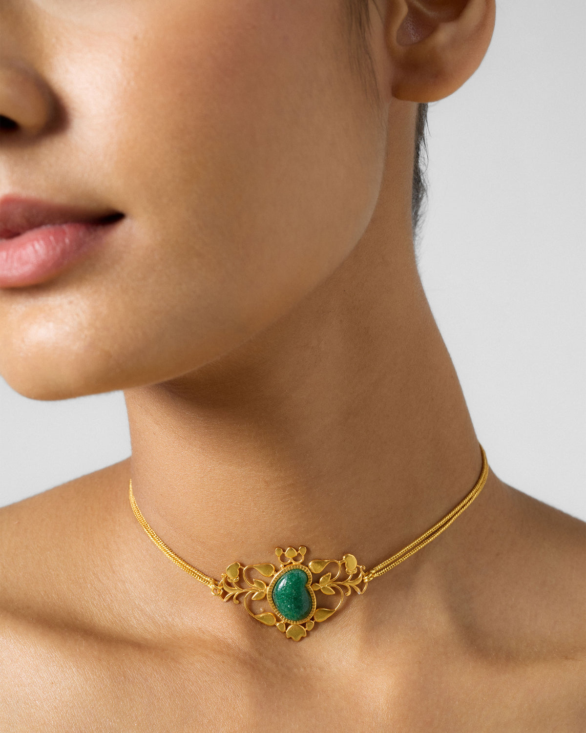 Gold Ambi choker with a green strawberry quartz motif worn at the neck.