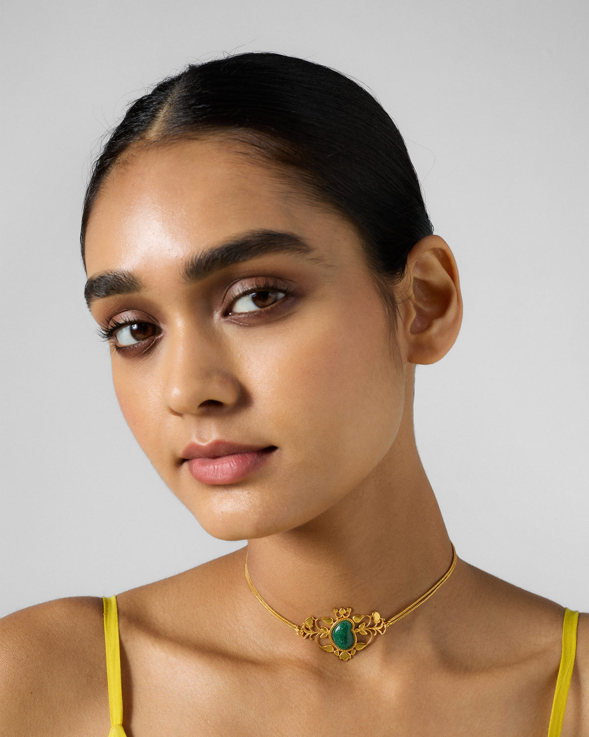 Person wearing a gold Ambi choker with a green stone motif.