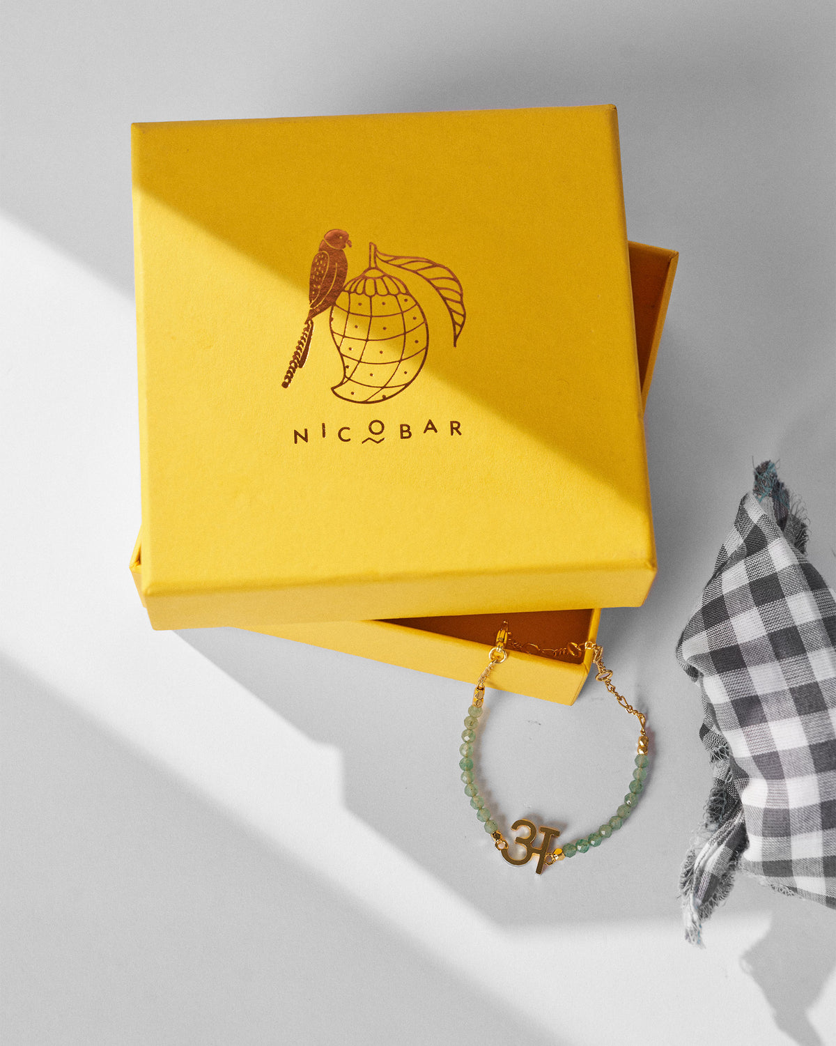 Akshar Bracelet (A) - Gold beside a yellow gift box.