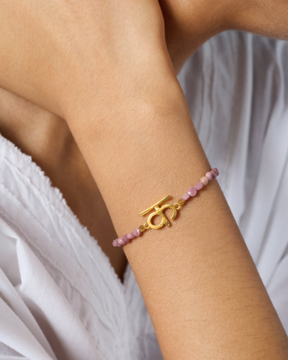 Gold Akshar K bracelet with dusty pink beads worn on a wrist.