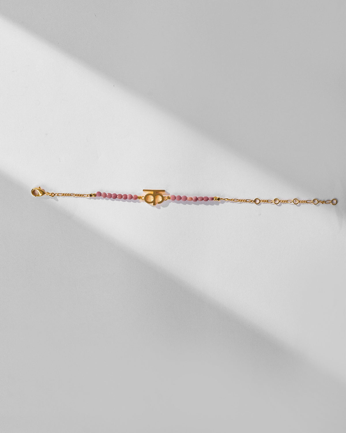 Gold Akshar K bracelet with dusty pink beads and an adjustable clasp.