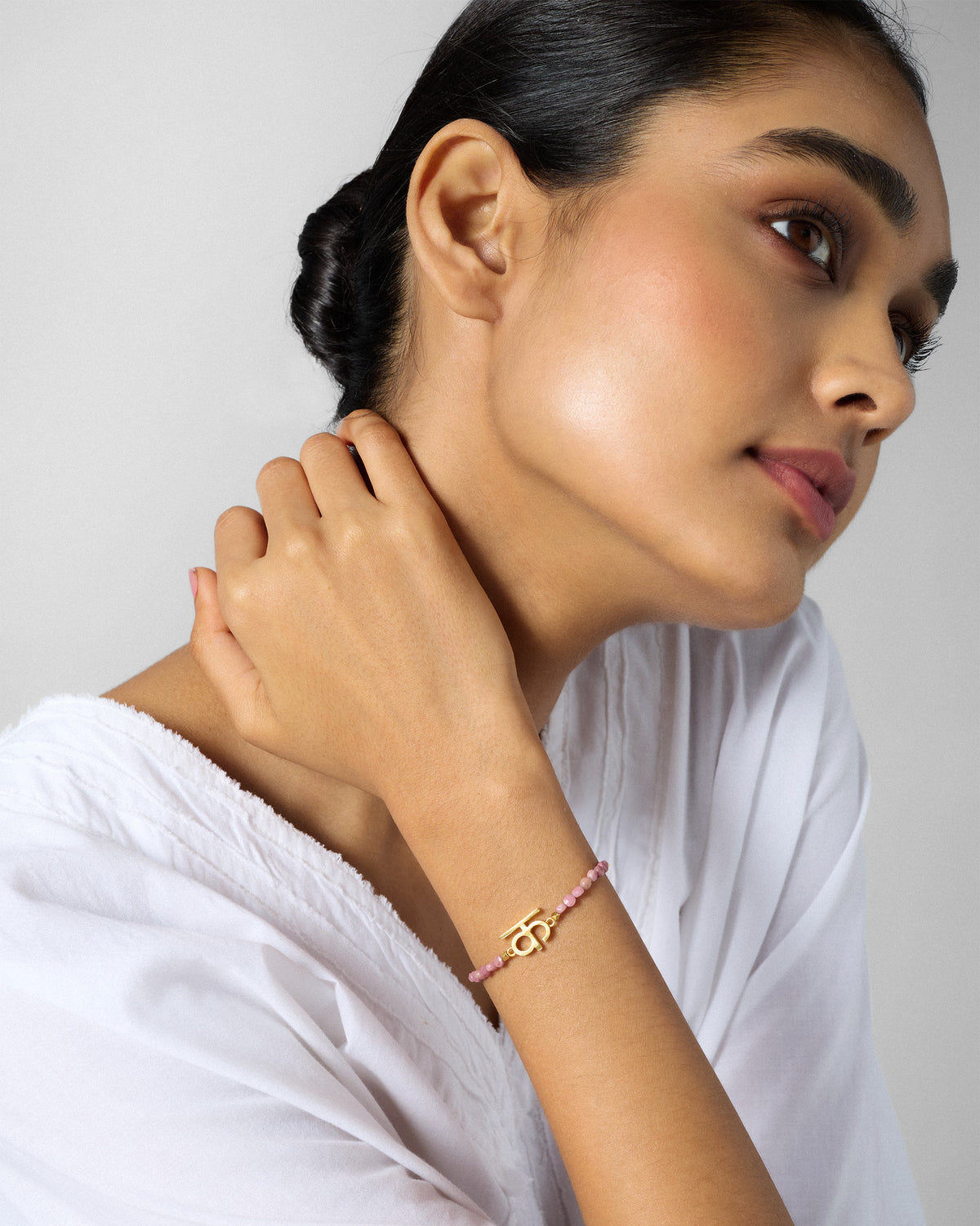 Side view of a gold Akshar K bracelet with dusty pink beads on a wrist.