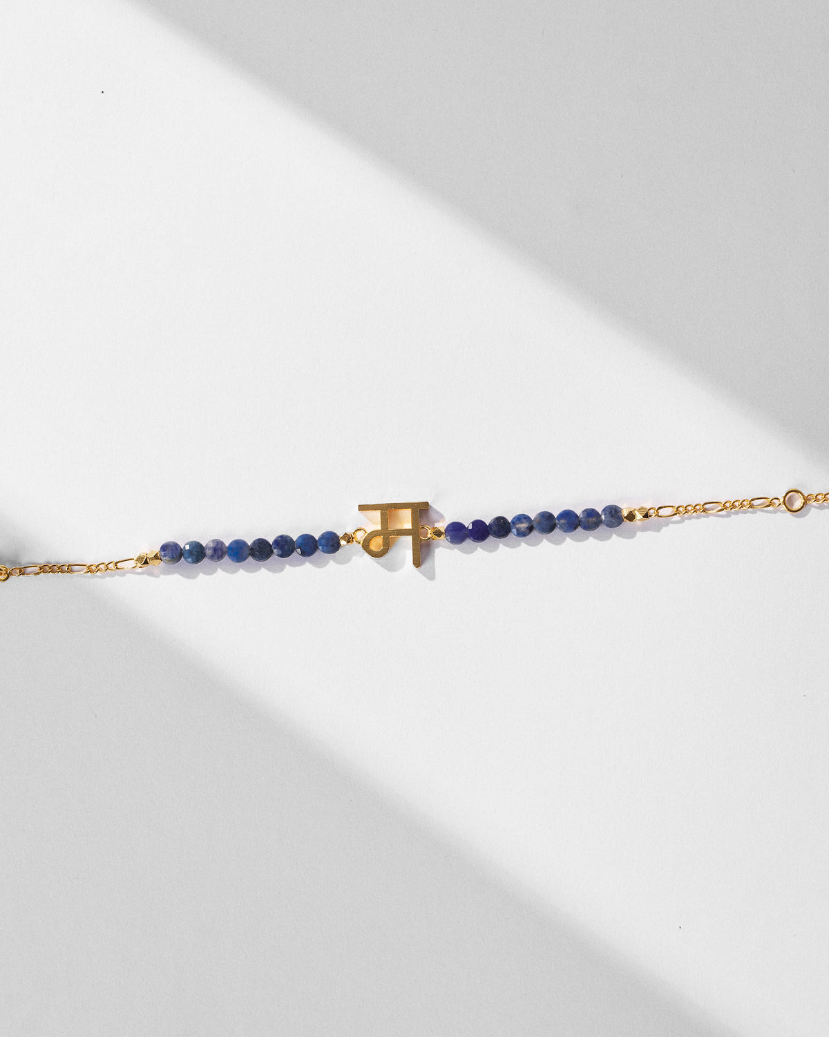 Angled view of Akshar Bracelet (M) - Gold with blue beads and a gold charm.