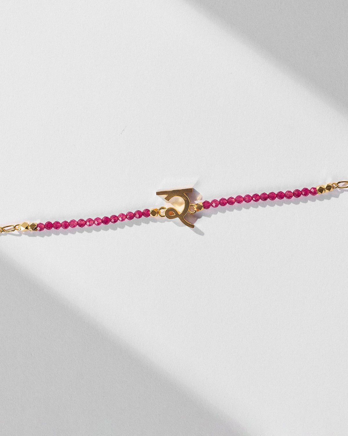 Close-up of Akshar Bracelet (R) - Gold showing its charm and pink beads.