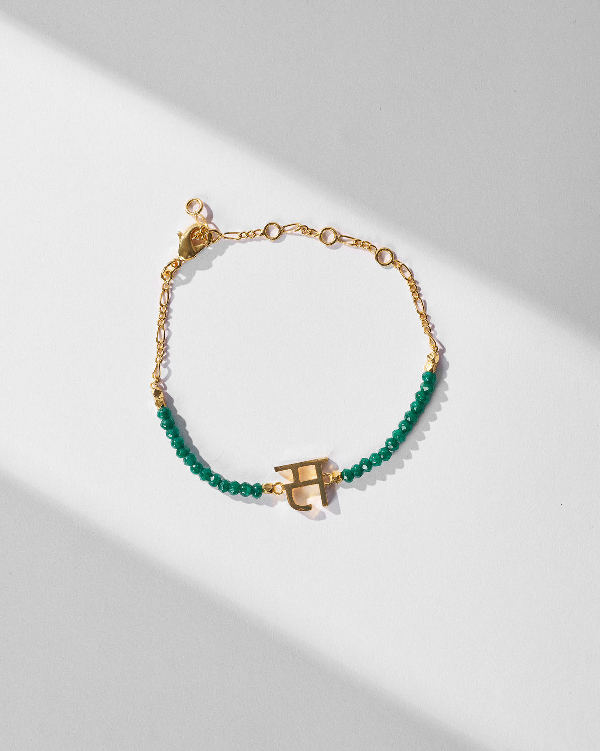 Akshar Bracelet (S) - Gold laid at an angle, with green beads and a gold charm.