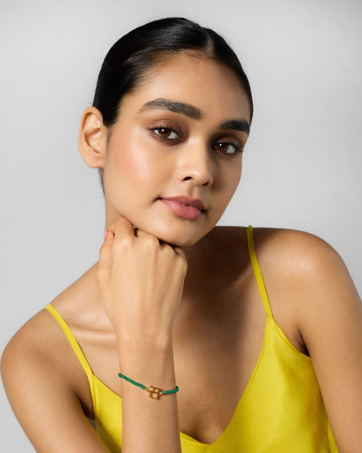 Person wearing Akshar Bracelet (S) - Gold with a hand raised near the chin.