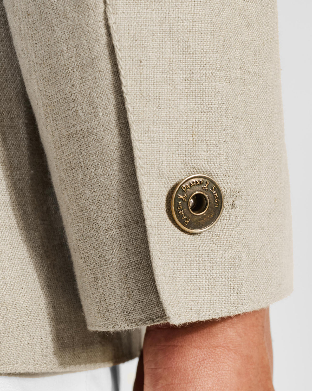 Close-up of a brass cuff button on a beige linen Tahr bandhgala.
