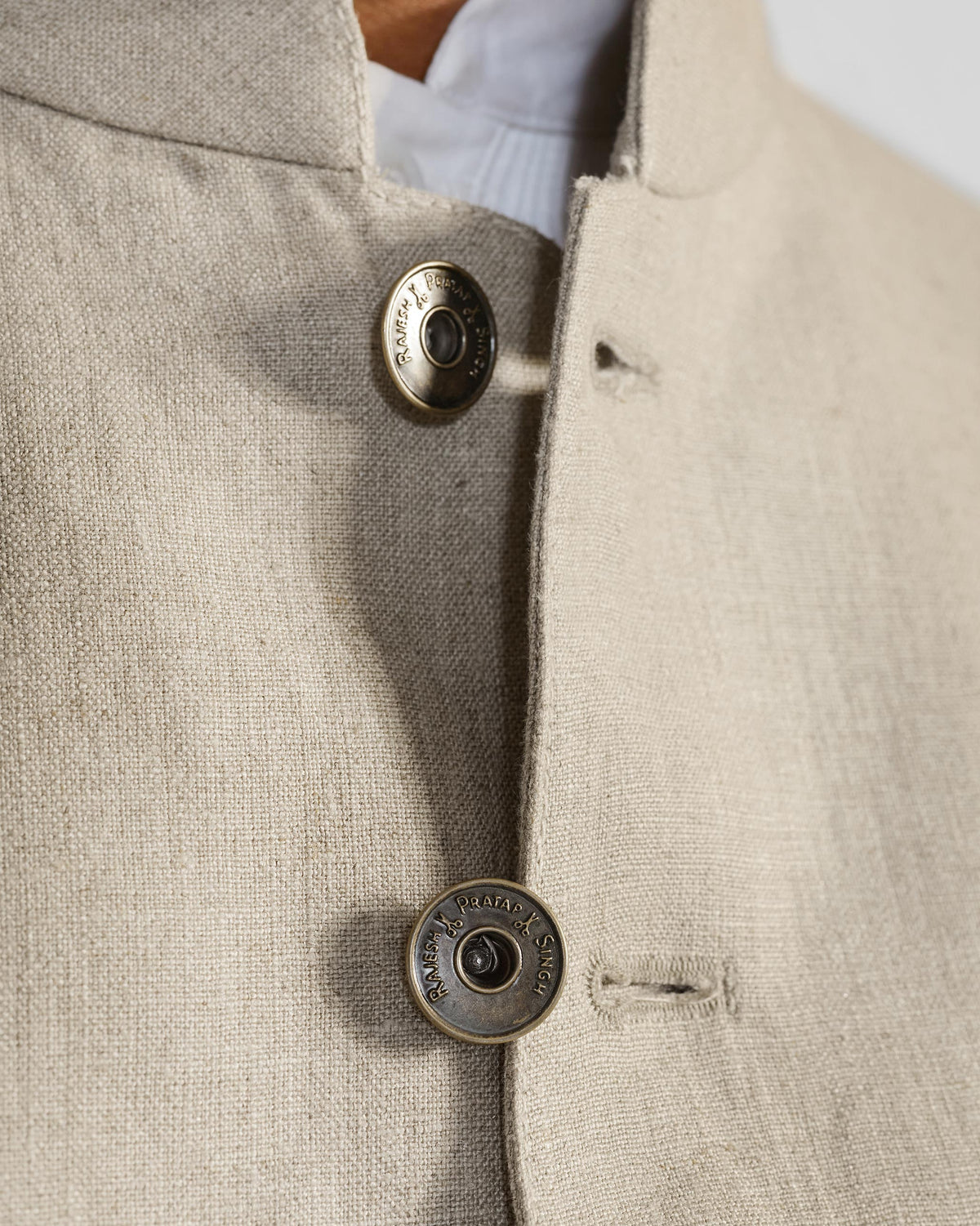 Close-up of brass buttons at the mandarin collar of a beige Tahr bandhgala.