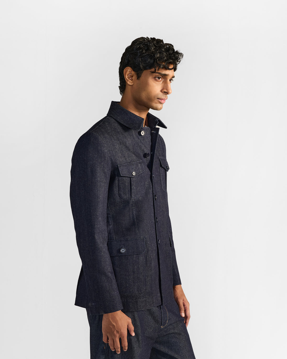Side view of an indigo denim Ibex travel jacket with flapped utility pockets.