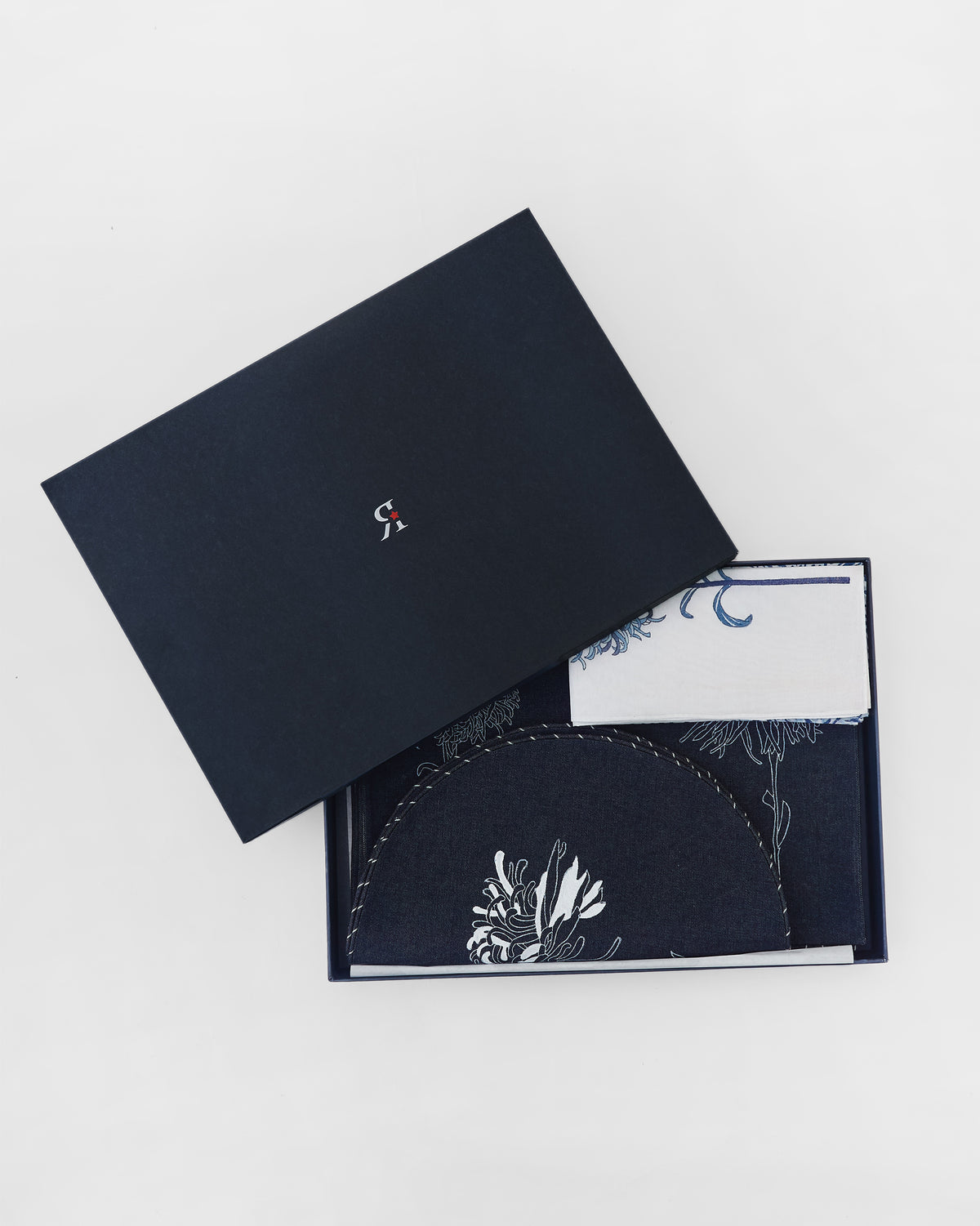 Open Chandramallika gift box revealing navy and white floral table linens.