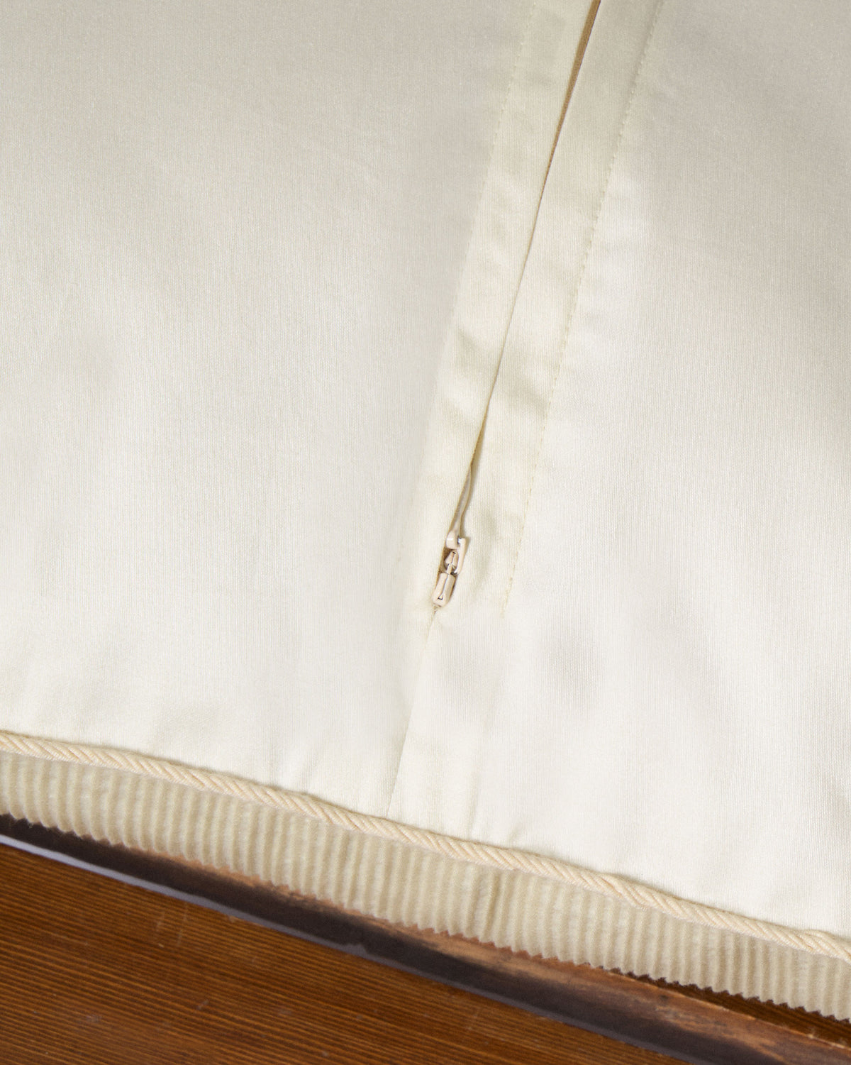 Close-up of the cream cushion's zip opening and corded piped edge.