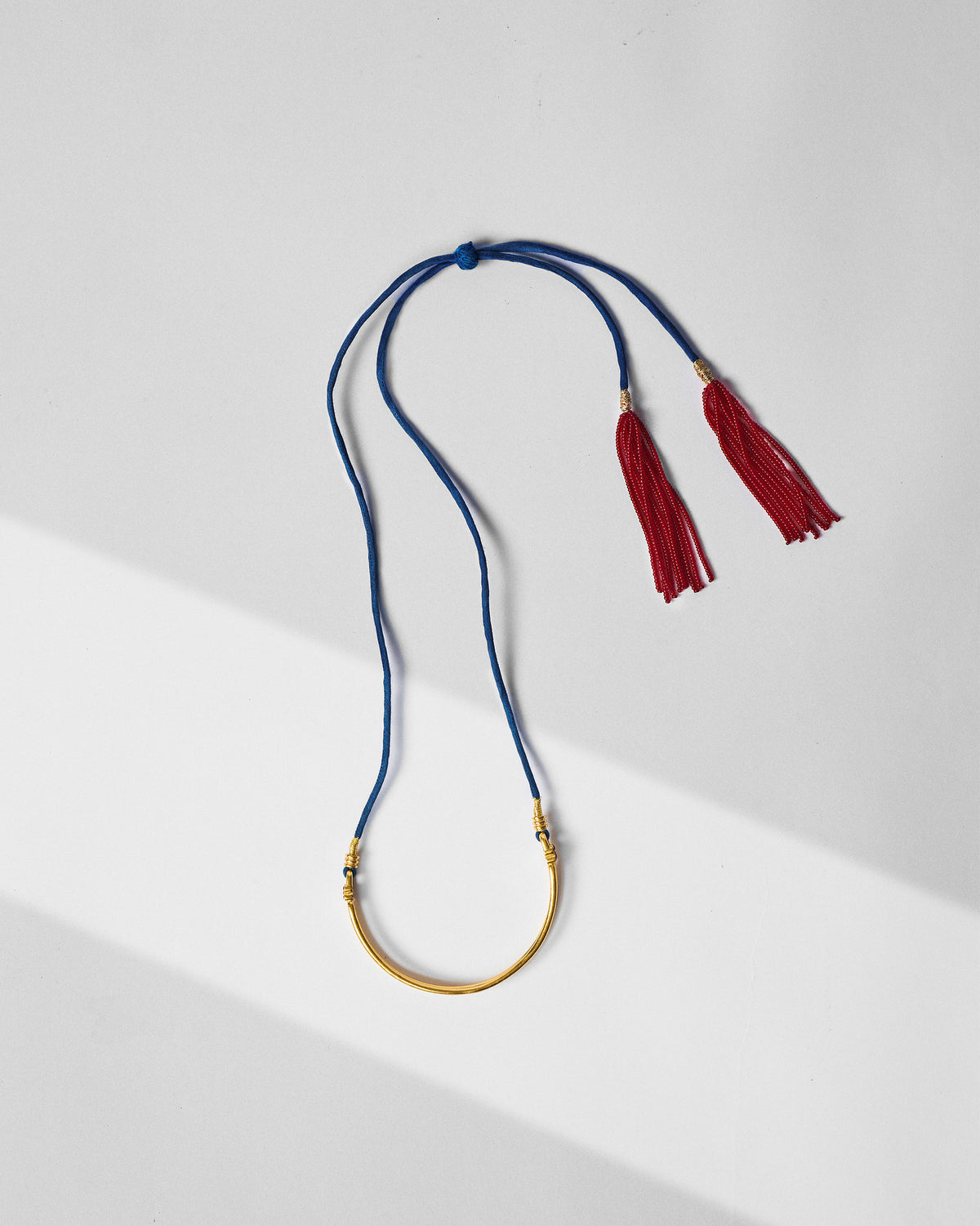 Gold baju bandh with blue cord and red tassels laid flat.