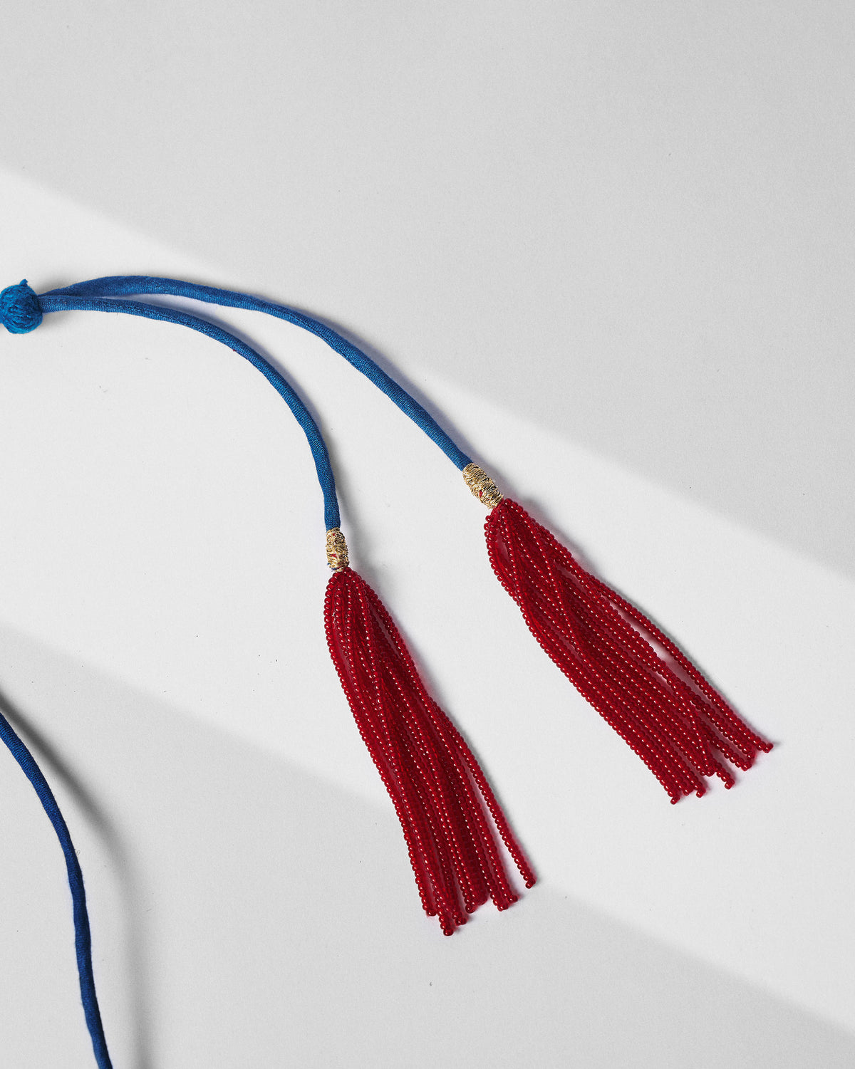 Close-up of red bead tassels on the blue cord of a gold baju bandh.