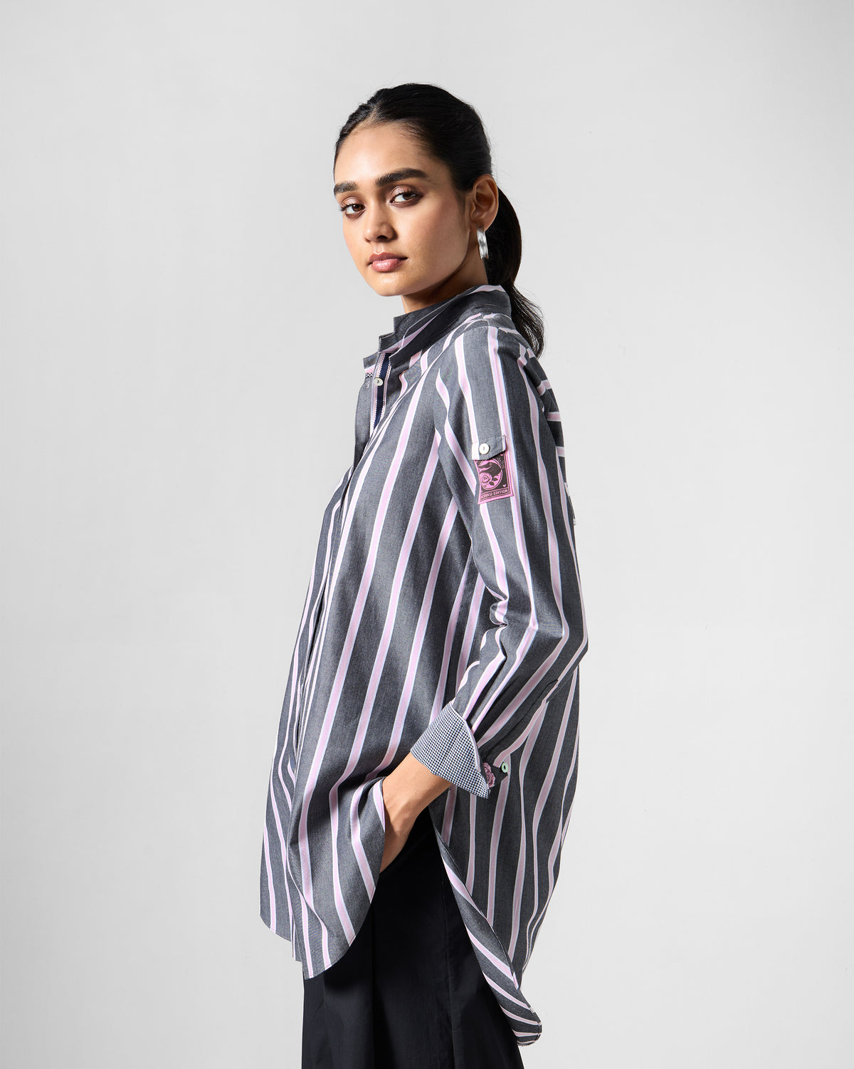 Side view of a long charcoal and pink striped Trench shirt with a curved hem.