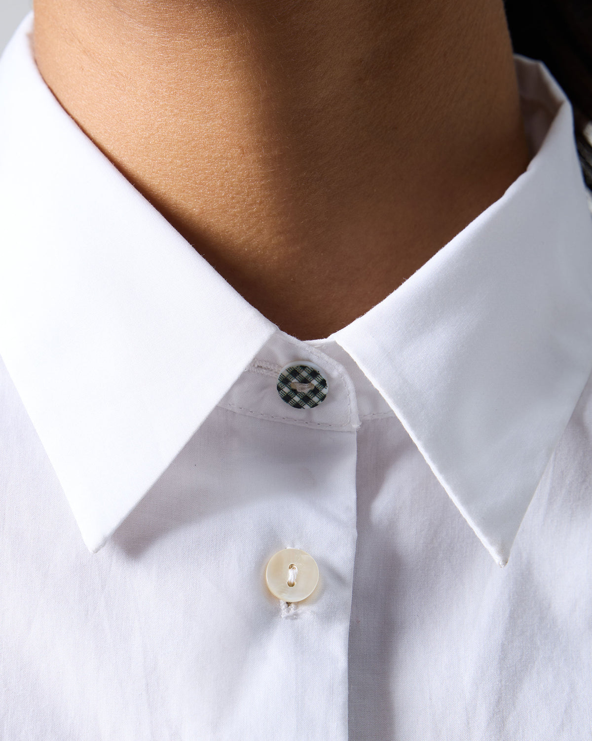 Close-up of a check button on a white Trench shirt collar.