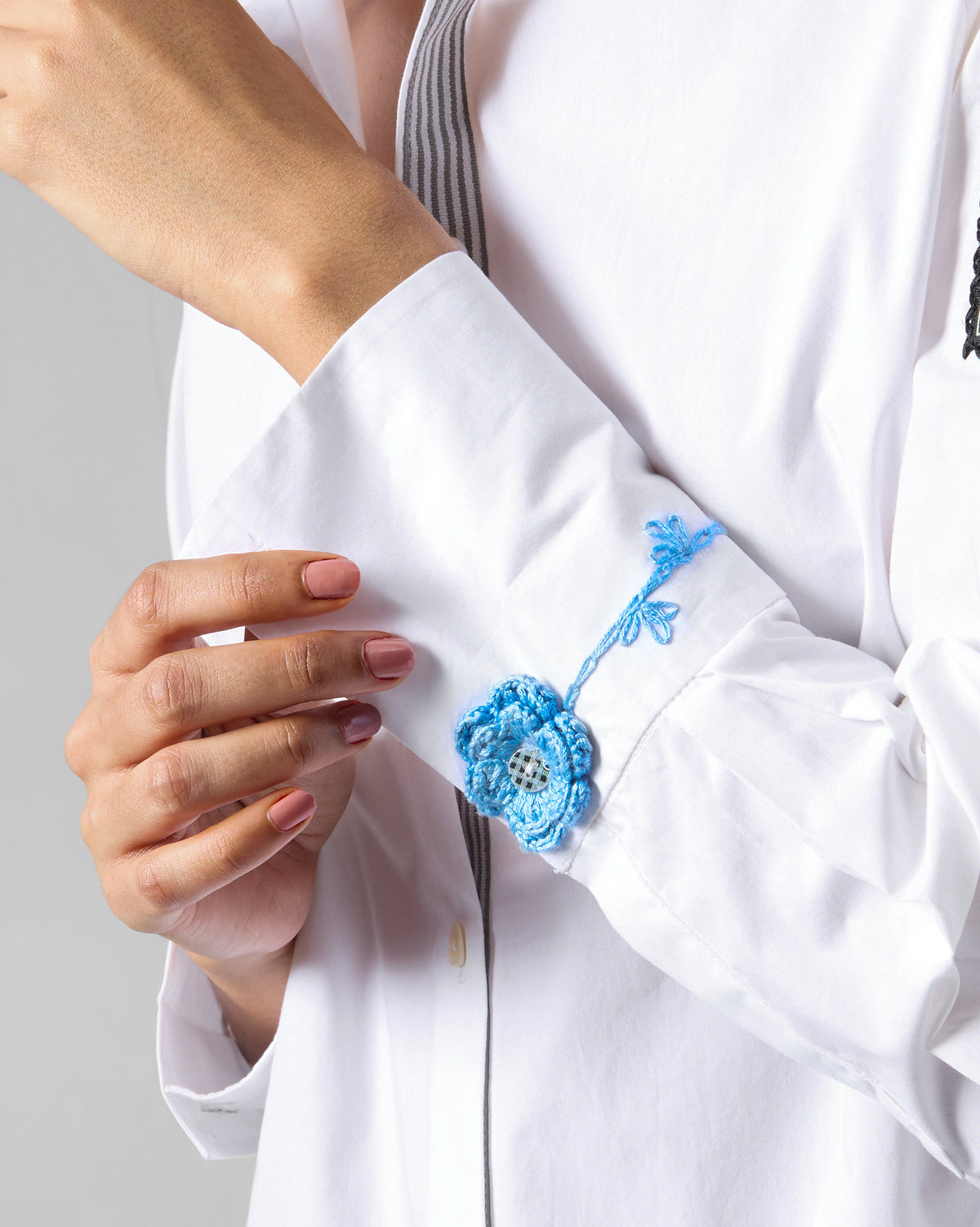 Close-up of a blue crochet flower on a white Trench shirt cuff.