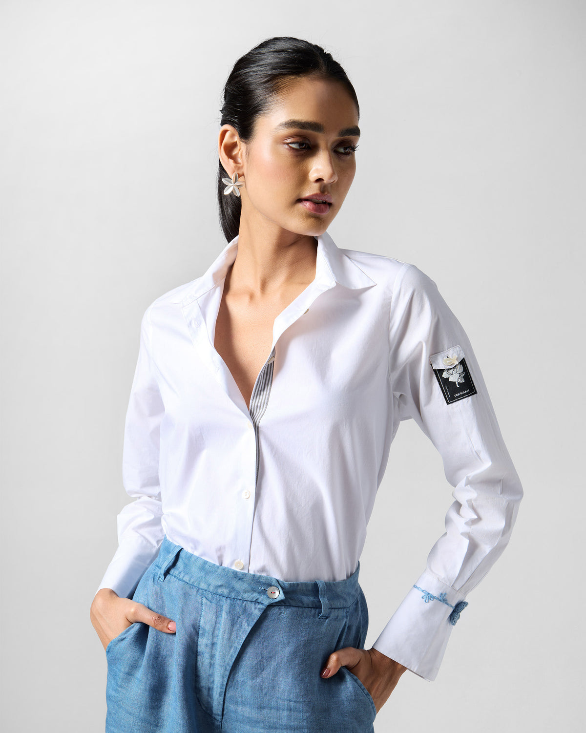 Person wearing a white Trench shirt with blue cuff embroidery.