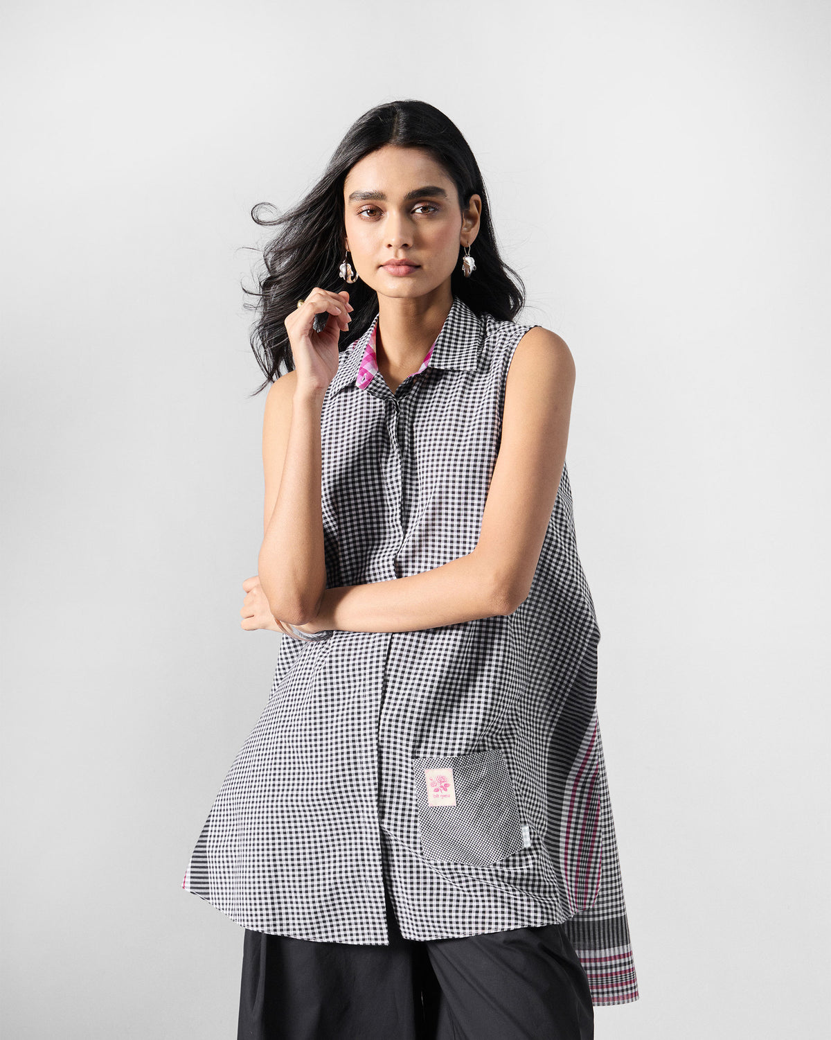 Person wearing a black and white check sleeveless tunic with a patch pocket.