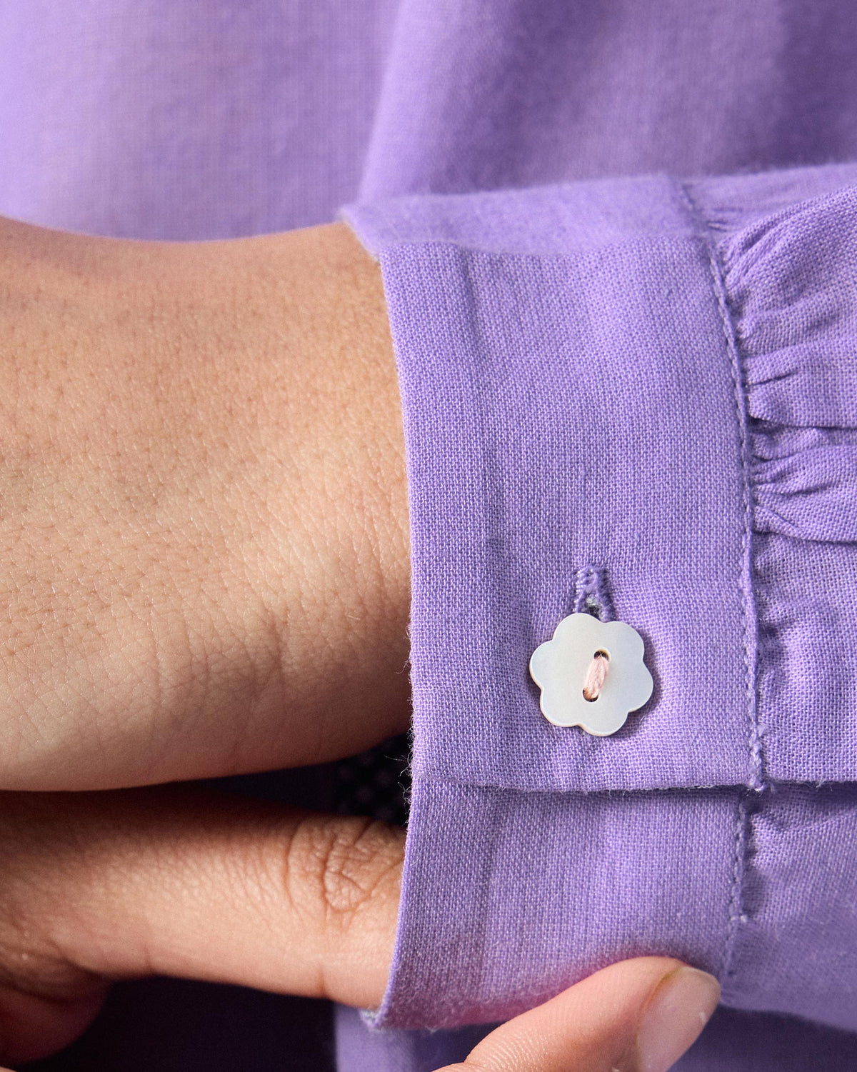 Close-up of a white flower button on the cuff of a lilac kurta.