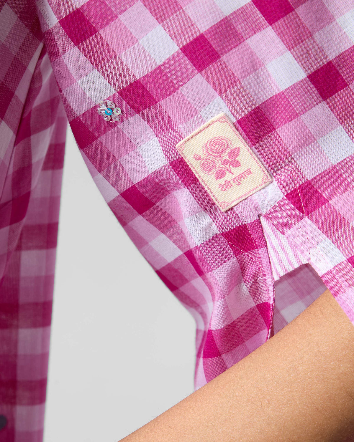 Close-up of a pink and white check Amaya tunic sleeve with a rose label.