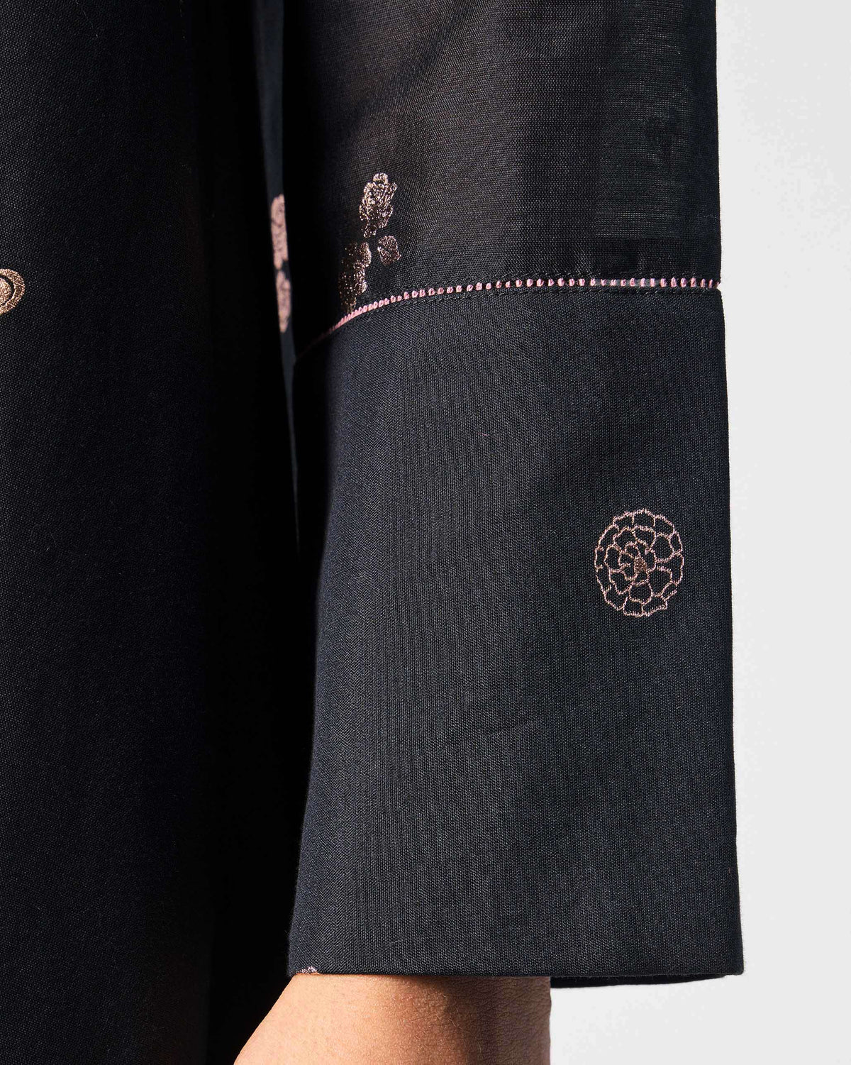 Close-up of pink motif and fagotting on a black V-Neck Flared dress sleeve.
