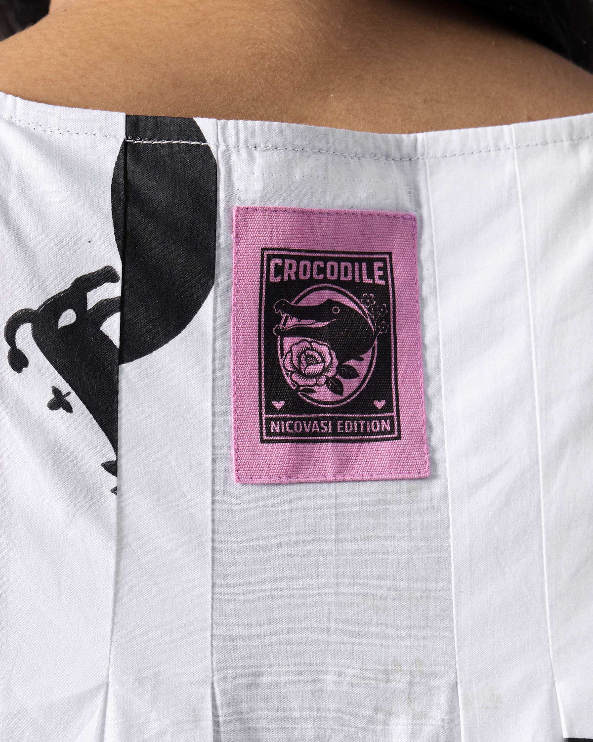 Close-up of a white dress with a pink crocodile patch at the neck.