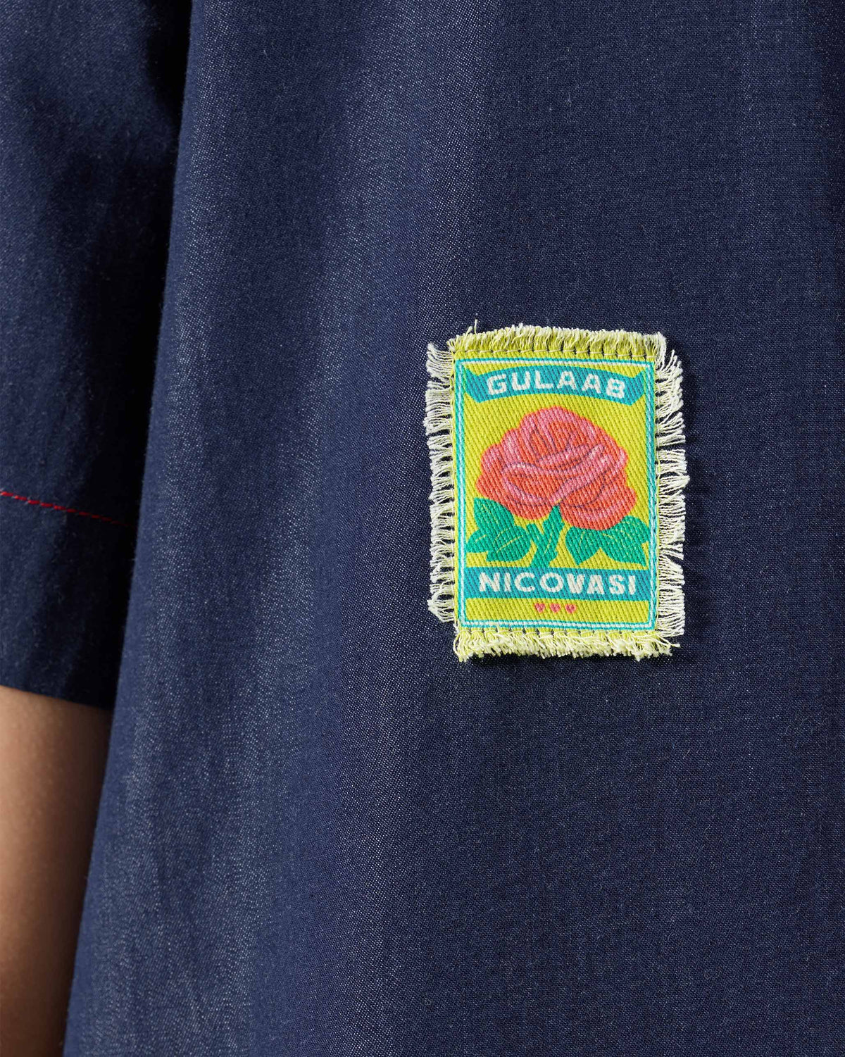 Close-up of a navy Peru jumpsuit with a rose patch labelled Gulaab Nicovasi.