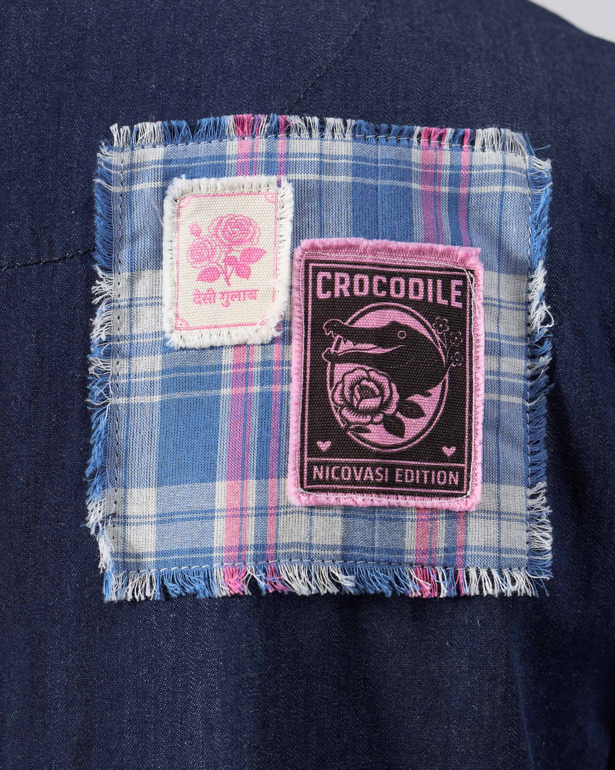 Close-up of a navy Peru jumpsuit with a plaid patch and Crocodile Nicovasi Edition badge.