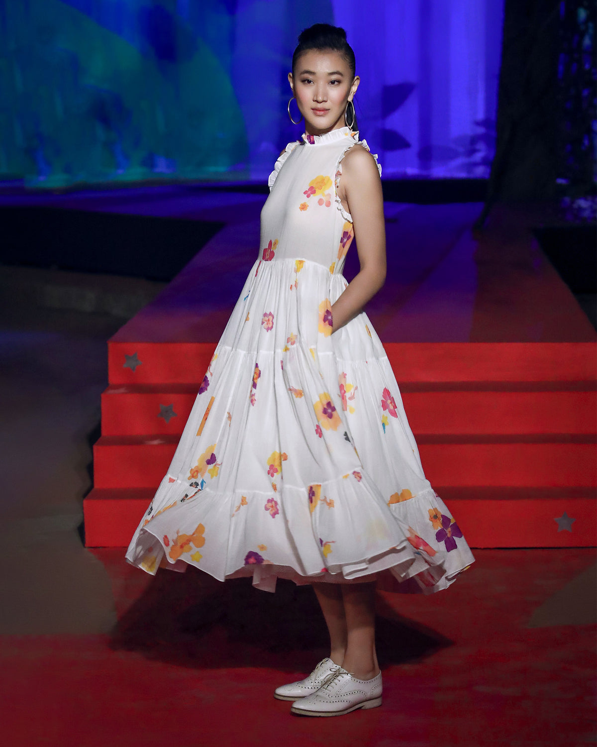 Person wearing an ivory floral Reah dress with a hand in the side pocket.