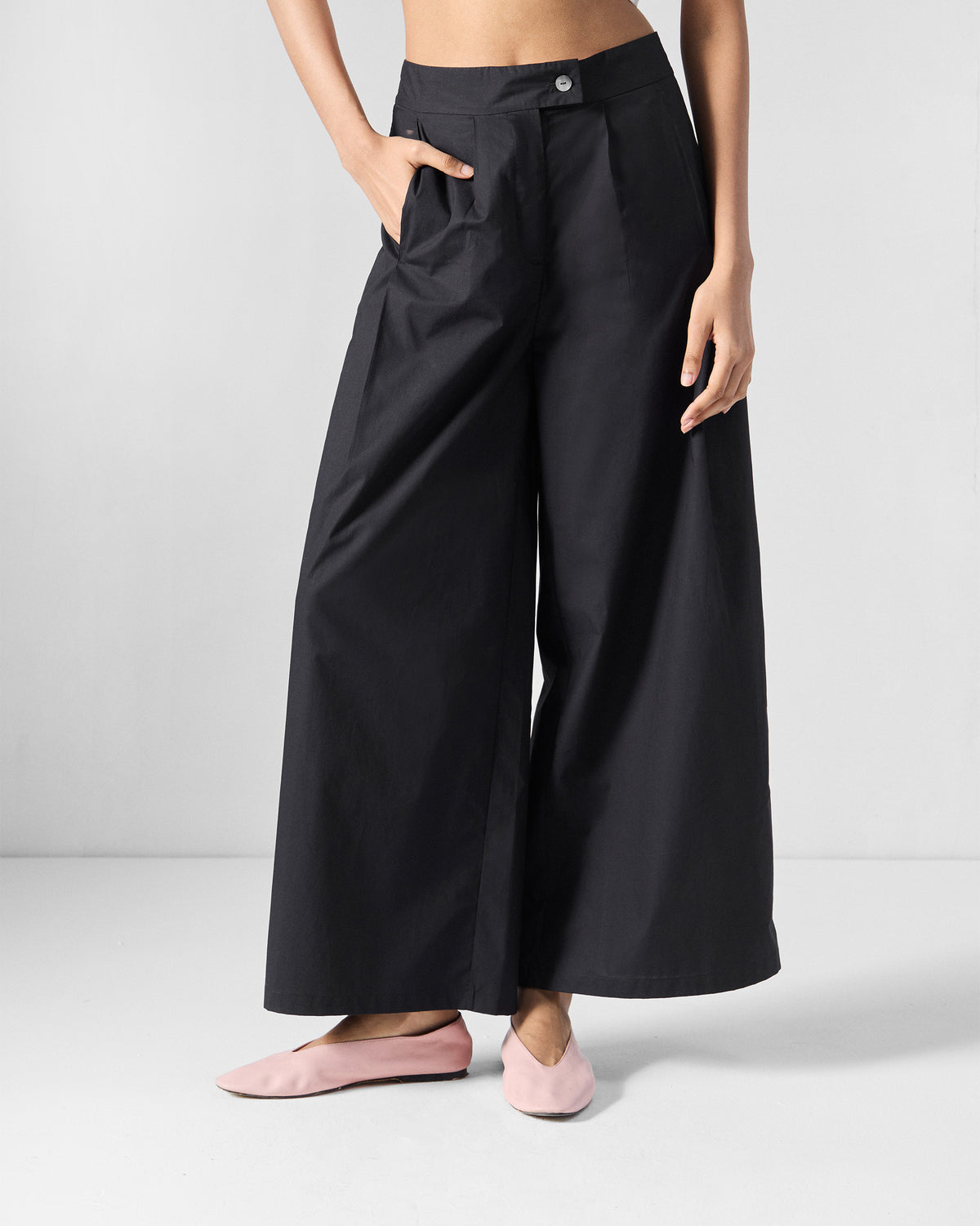 Person wearing black wide-leg Bank pants with a white button waist.