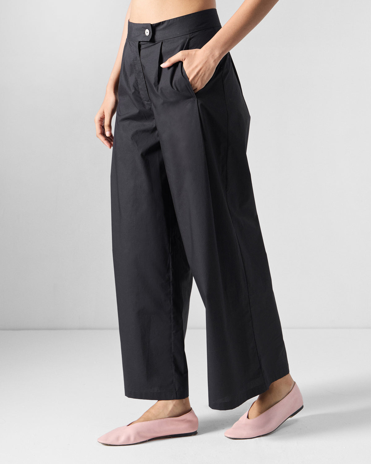 Angled view of black wide-leg Bank pants showing the pleated waist.