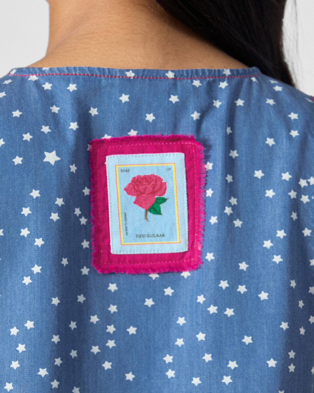 Close-up of a blue star-print dress with a pink rose patch.