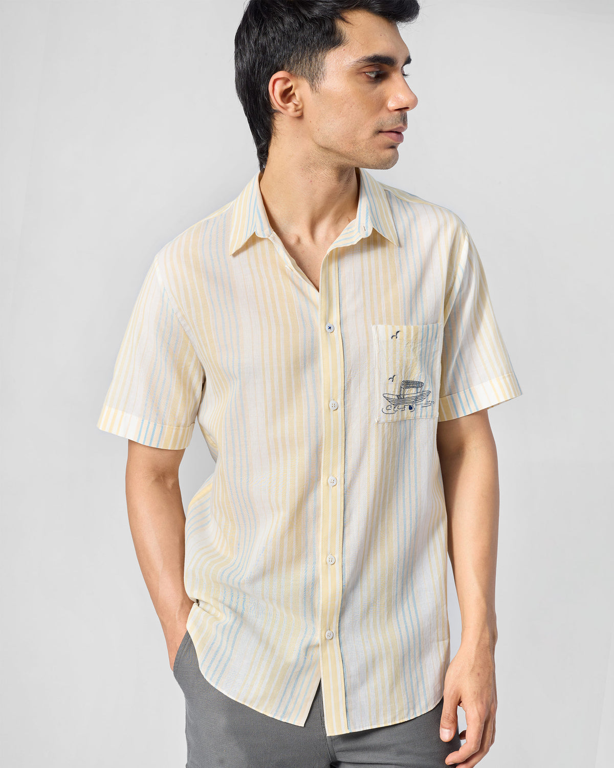 Person wearing a yellow and blue striped Flow Half Sleeve Shirt with boat embroidery on the pocket.