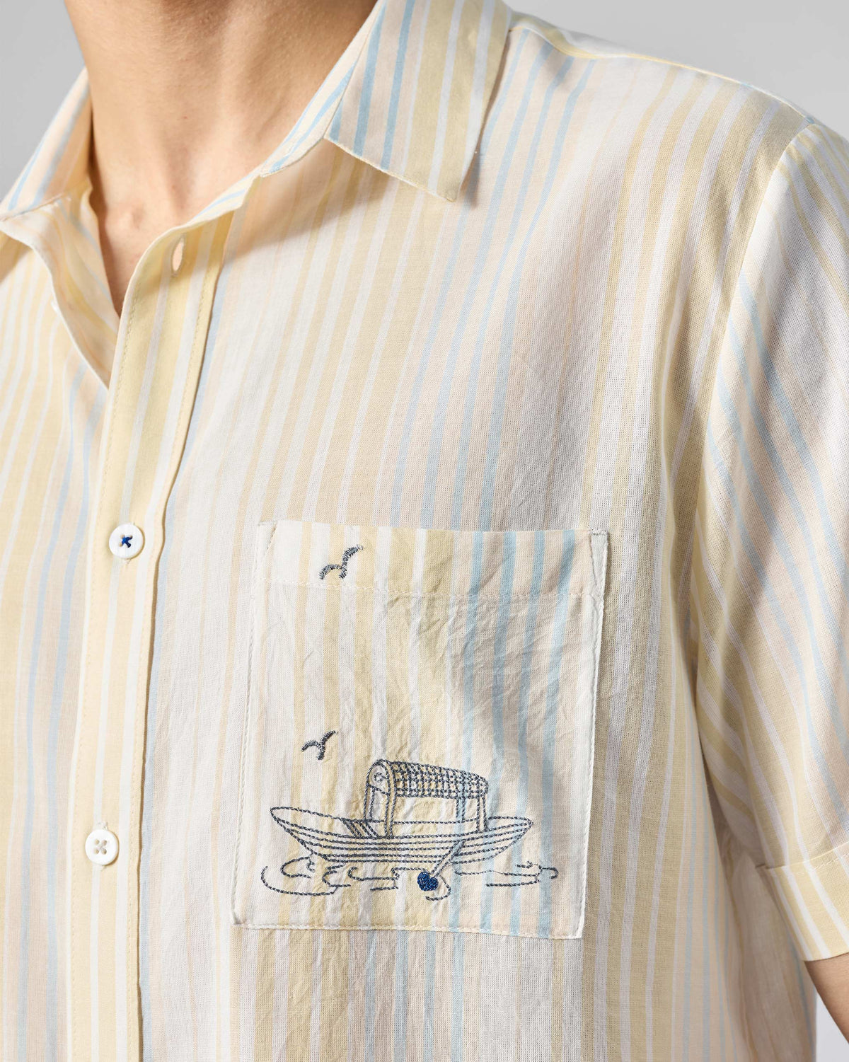 Close-up of boat embroidery on the pocket of a yellow and blue striped Flow Half Sleeve Shirt.